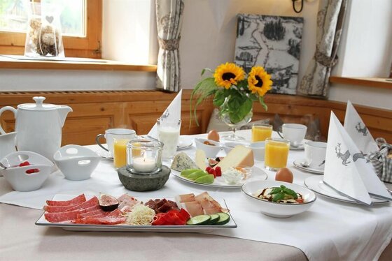 Gedeckter Frühstückstisch mit Wurst, Käse, Obst, Säften und Sonnenblumen in einer rustikalen Stube.