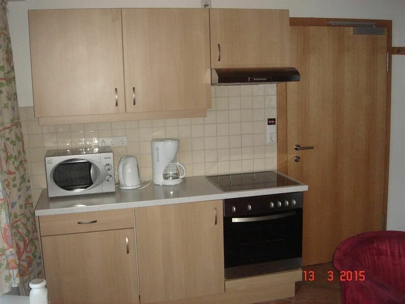 Kleine Küchenzeile aus hellem Holz mit Herd, Backofen, Mikrowelle und Kaffeemaschine.