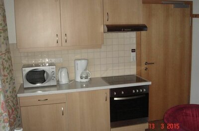 Kleine Küchenzeile aus hellem Holz mit Herd, Backofen, Mikrowelle und Kaffeemaschine.