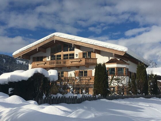 Alpines Wohnhaus mit schneebedecktem Dach und Holzbalkonen vor blauem Himmel.