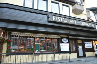 Außenansicht des Restaurants Zum Zinnkrug mit dunkler Holzfassade und beleuchteten Fenstern.
