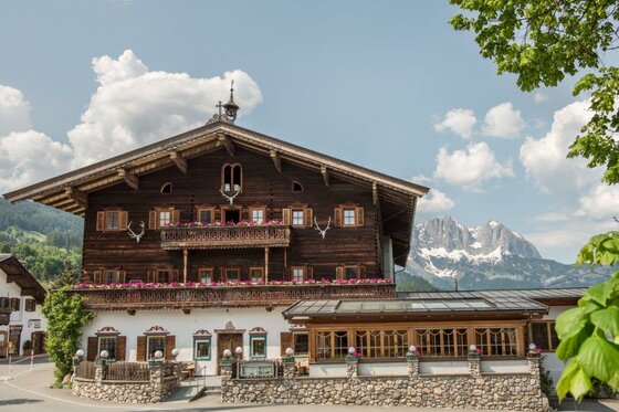 Traditionelles Holzgebäude mit Blumenbalkonen vor schneebedeckten Berggipfeln.
