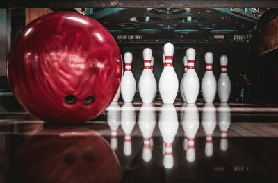 Kegelbahn Reith Rote Bowlingkugel im Vordergrund vor aufgestellten weißen Pins auf einer Bowlingbahn.