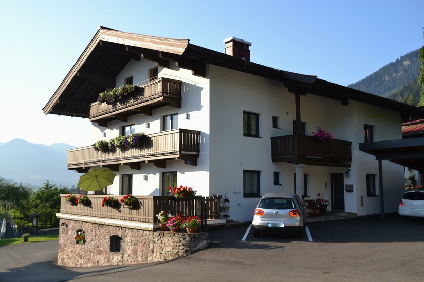 Haus Eugenie in Berglandschaft Zweistöckiges weißes Alpenhaus mit Holzbalkonen, Blumenschmuck und geparktem Auto davor.