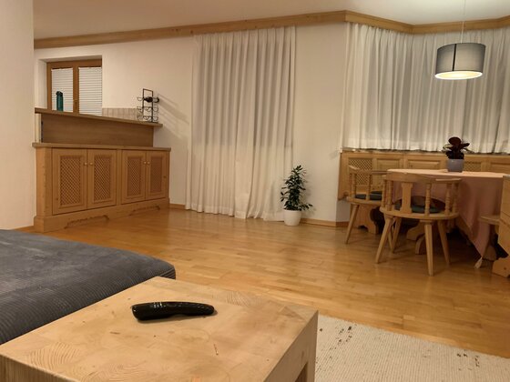 Wohnzimmer mit hellem Parkettboden, Holzmöbeln, einer Sitzecke und einer Bar.