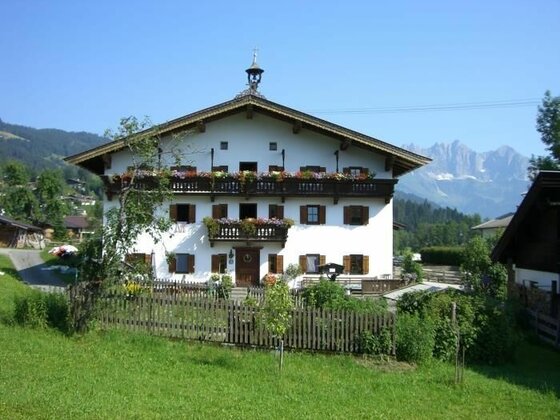 Alpenländisches Bauernhaus mit Blumenbalkonen vor Gebirgskulisse.