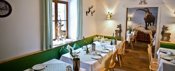 Frühstücksraum im Hotel Gamshof Eingedeckte Tische in einem Frühstücksraum mit alpiner Dekoration und grünen Sitzbänken.