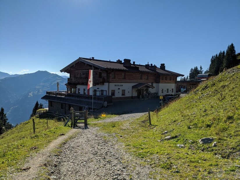 Berggasthaus Bichlalm Großes Berggasthaus aus Holz und Stein an einem Schotterweg vor Gebirgspanorama.