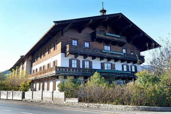 Alpiner Pöllhof im Sommer Großes alpines Holzhaus mit weißer Fassade im Erdgeschoss und umlaufenden Holzbalkonen an einer Straße.