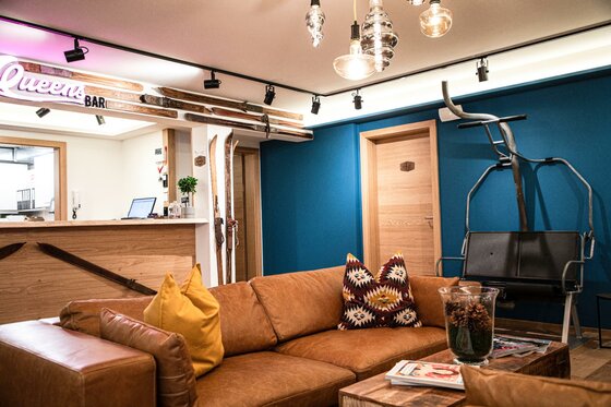 Hostel-Lounge Safestay Kitzbühel Loungebereich mit braunem Ledersofa, Holztisch und einem umgebauten Sessellift als Sitzgelegenheit vor blauer Wand.