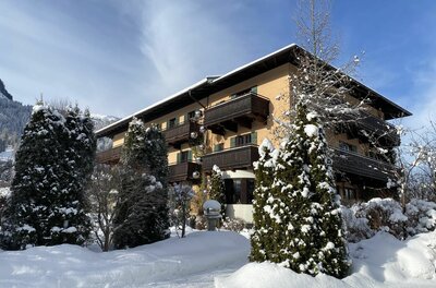 Mehrstöckiges Hotelgebäude mit Holzbalkonen in einer verschneiten Winterlandschaft unter blauem Himmel.