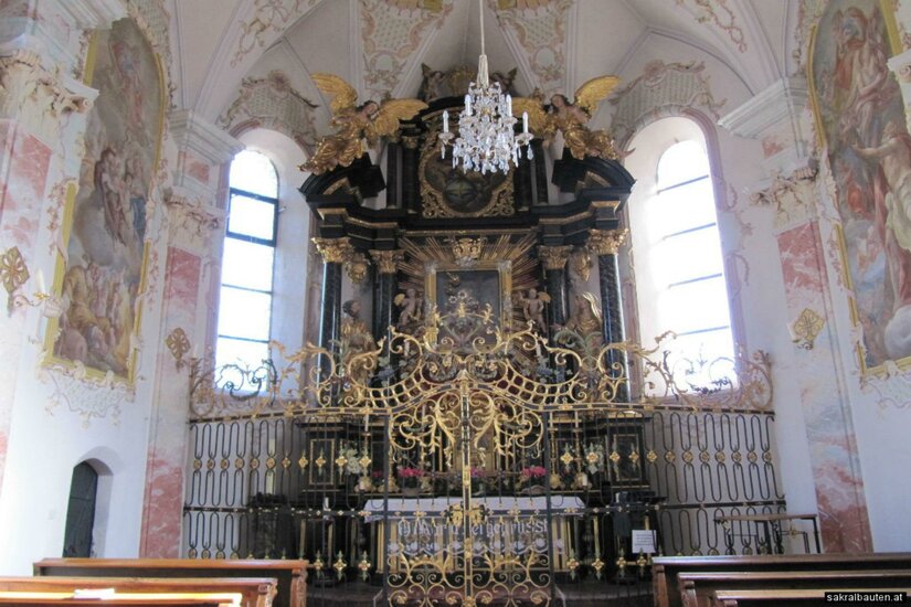 Ein beeindruckender Kirchenaltar mit kunstvoller Verzierungen und einem großen Kronleuchter. Helle Fenster lassen viel Licht in den Raum strömen.