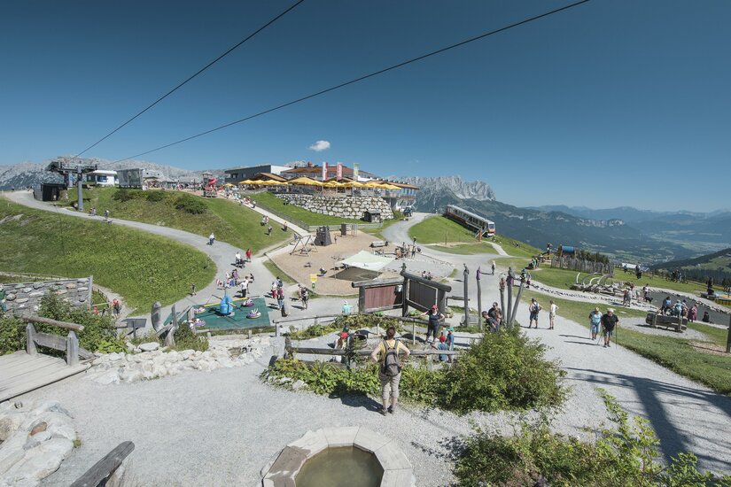 Ellmi's Zauberwelt Ein malerischer Bergort mit vielen Besuchern und klar blauem Himmel. Die Umgebung ist grün und einladend, ideal für Outdoor-Aktivitäten.