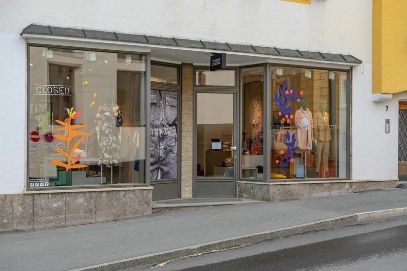 Closed Store Kitzbühel Schaufensterfront eines Bekleidungsgeschäfts mit Mannequins und farbigen Grafiken an der Glasfläche.