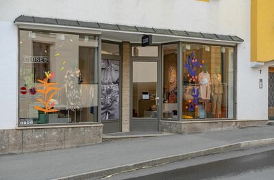 Schaufensterfront eines Bekleidungsgeschäfts mit Mannequins und farbigen Grafiken an der Glasfläche.