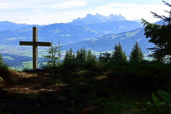Aussichtspunkt am Kaiserblickweg Holzkreuz auf einer bewaldeten Anhöhe mit Blick auf ein weites Tal und ferne Gebirgsketten.
