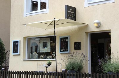 Außenansicht eines Schmuckgeschäfts mit Schaufenster, Sonnenschirm und Lavendel im Vordergrund.