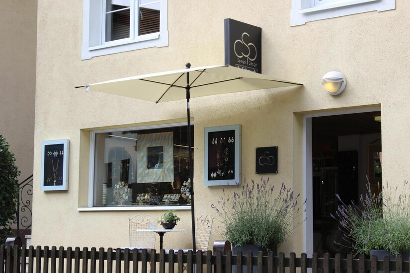 Spiegel Design Schmuckgeschäft Außenansicht eines Schmuckgeschäfts mit Schaufenster, Sonnenschirm und Lavendel im Vordergrund.