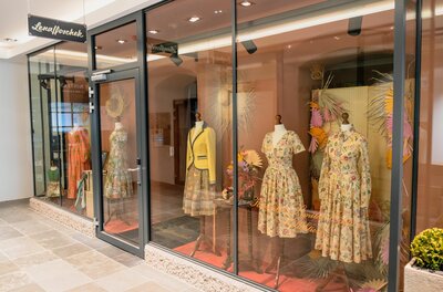 Schaufenster mit Kleidern auf Mannequins hinter einer Glasfront.
