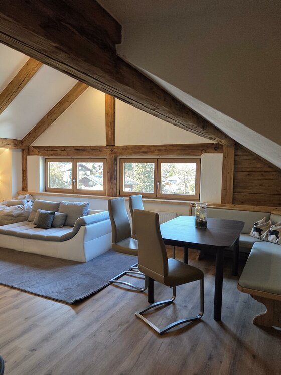 Wohnbereich Resi´s Streifblick Lodge Ein modernes Wohnzimmer mit Holzbalken und großen Fenstern. Es gibt eine gemütliche Sofagarnitur und einen Esstisch mit Stühlen.