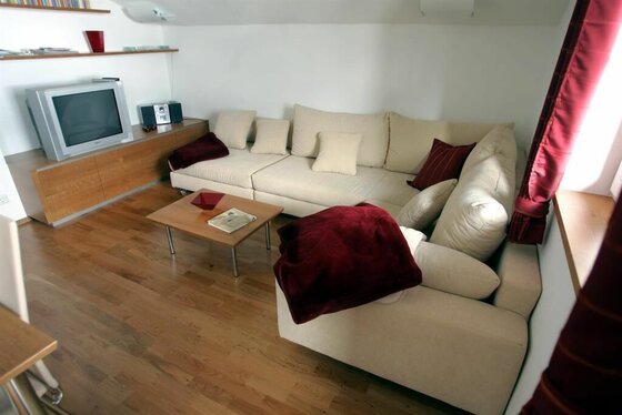 Wohnzimmer mit hellem Ecksofa, Holztisch und Fernseher auf einem Sideboard.