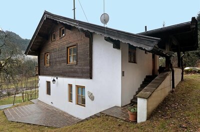 Zweistöckiges Haus mit weißer Fassade im Erdgeschoss und dunkler Holzverkleidung im Obergeschoss.
