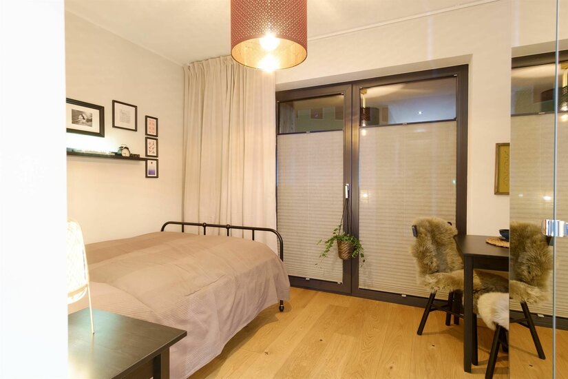 Modernes Schlafzimmer mit Metallbett, Holzboden und einem kleinen Tisch mit Fellstühlen vor einem Fenster.