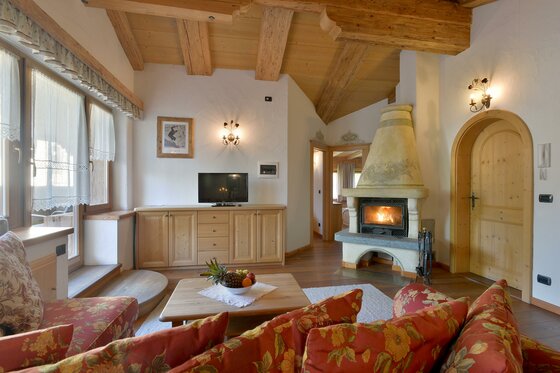 Rustikaler Wohnraum mit Holzbalkendecke, Kaminfeuer, TV und gemusterten Sofas.