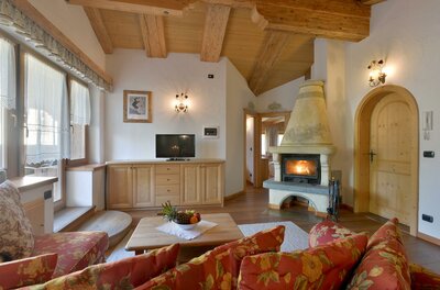 Rustikaler Wohnraum mit Holzbalkendecke, Kaminfeuer, TV und gemusterten Sofas.