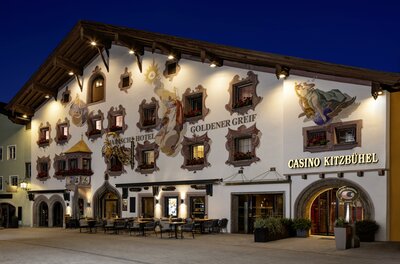 Ein traditionelles Gebäude mit bemalten Fassaden und vielen Fenstern. Das Kasino Kitzbühel ist deutlich erkennbar und die Atmosphäre ist einladend.