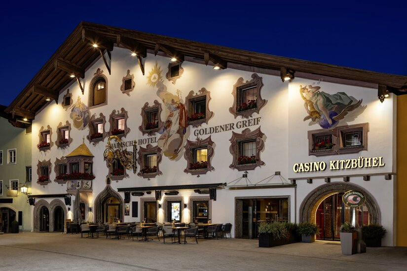 Casino Ein traditionelles Gebäude mit bemalten Fassaden und vielen Fenstern. Das Kasino Kitzbühel ist deutlich erkennbar und die Atmosphäre ist einladend.