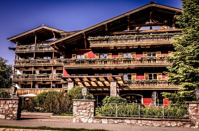 Ein schönes Holzhaus im Alpenstil mit mehreren Balkonen. Umgeben von Bäumen und grünen Pflanzen.