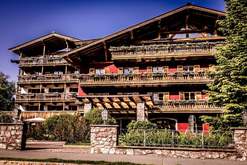 Ein schönes Holzhaus im Alpenstil mit mehreren Balkonen. Umgeben von Bäumen und grünen Pflanzen.