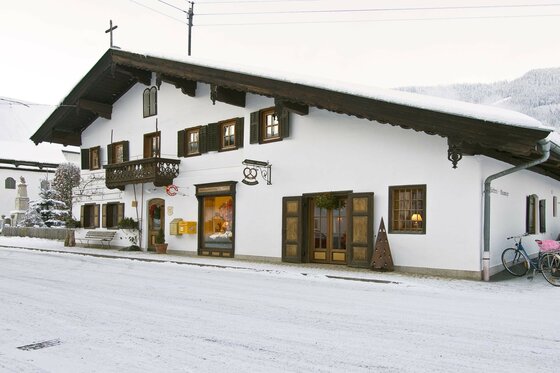 Alpenländisches Gebäude mit weißer Fassade und dunklem Holzdach in verschneiter Umgebung.