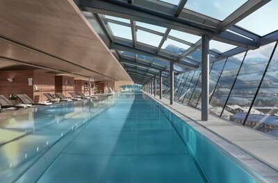 Hallenbad im Lebenberg Schlosshotel Langes Hallenbad mit Glasfront, Liegestühlen und Blick auf die verschneiten Alpen.