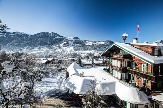 Verschneites Hotel Tennerhof in alpiner Landschaft mit Blick auf Kitzbühel und die Berge bei blauem Himmel.