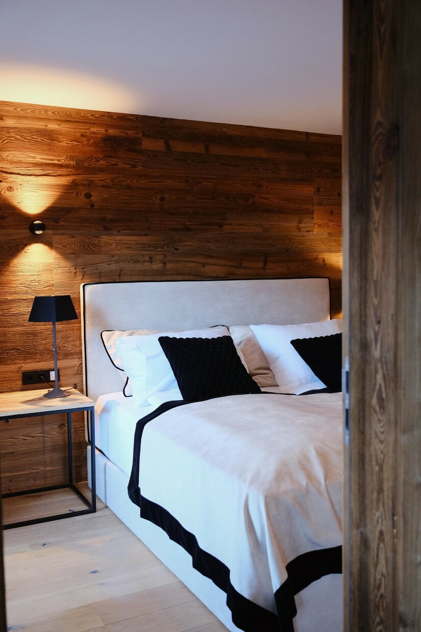 Modernes Doppelbett vor einer Wand aus dunklem Altholz mit Nachttischlampe.