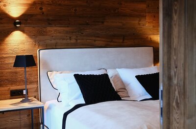 Modernes Doppelbett vor einer Wand aus dunklem Altholz mit Nachttischlampe.