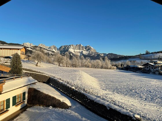 Verschneite Wiese mit Blick auf das Gebirgsmassiv des Wilden Kaisers unter blauem Himmel.
