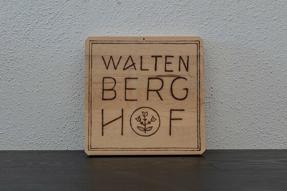 Ein aus Holz gefertigtes Schild mit der Aufschrift „Walten Berg Hof“. Es zeigt eine einfache, rustikale Gestaltung.