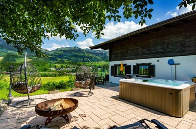 Terrasse mit Whirlpool, Hängesesseln und Feuerschale vor Bergpanorama.