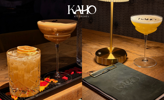 Cocktails im KAHO Kitzbühel Drei verschiedene Cocktails auf einer Bartheke und einem Holztisch neben einer Tischlampe.