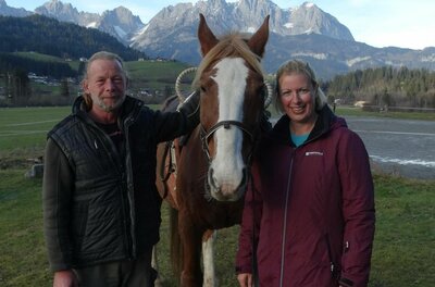 Gut Kohlhofen Reitangebot Ein Mann und eine Frau stehen neben einem braunen Pferd vor einer Bergkulisse.