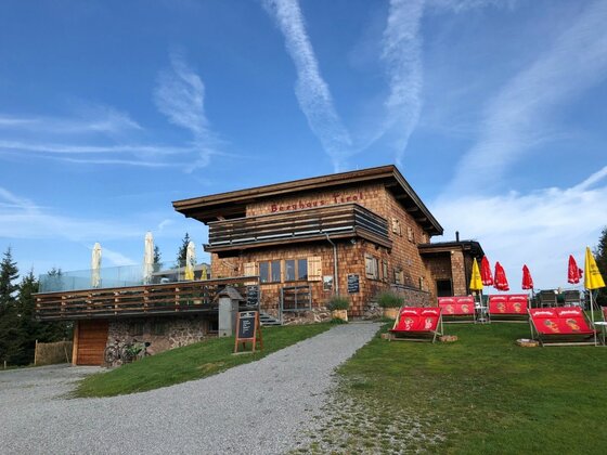 Holzhütte mit Terrasse, Sonnenschirmen und Liegestühlen vor blauem Himmel.