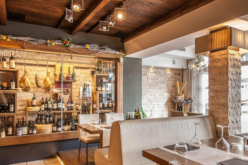 Innenansicht eines Restaurants mit Weinfächern, Steinsäule und eingedeckten Tischen.