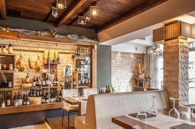 Innenansicht eines Restaurants mit Weinfächern, Steinsäule und eingedeckten Tischen.