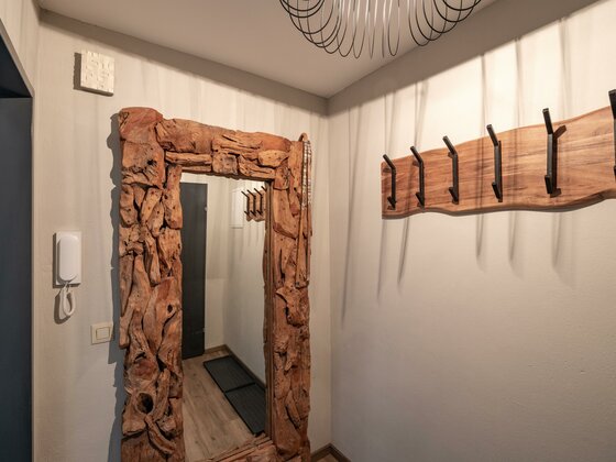 Garderobe im Appartement Hafkamp Flur mit großem Altholzspiegel und einer Wandgarderobe aus Holz mit schwarzen Metallhaken.