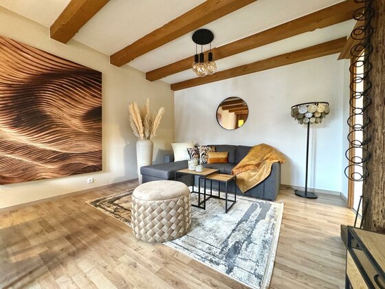 IMG_5271 Large Ein modernes Wohnzimmer mit einer bequemen Sofa-Ecke und einer eleganten Lampe. Die Wände sind hell, und es gibt ein großes Wandbild sowie einen runden Tisch im Zentrum des Raumes.