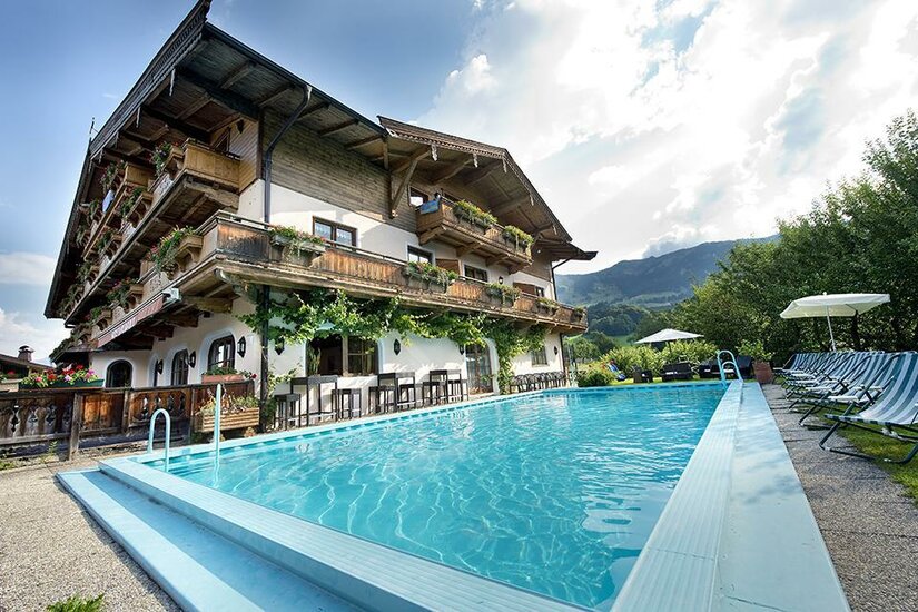 Poolview Hotel Alpenhof Außenpool vor einem mehrstöckigen alpinen Hotelgebäude mit Holzbalkonen und Liegestühlen.