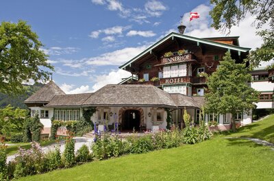 Außenansicht des Hotel Tennerhof mit Holzfassade, Blumengarten und österreichischer Flagge unter blauem Himmel.